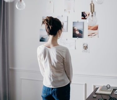 mobile image of woman looking at inspiration ideas on paper that 
        are stuck to the wall with triple-image